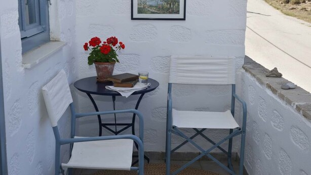 A small outdoor seating area with two chairs, a table with a potted plant and a book, and a framed picture on the wall. - Santorini Stay With Hot Tub (Patmos)