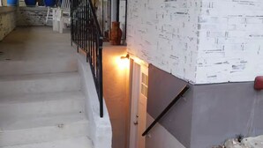 Un escalier avec une rampe noire, une porte en bas et un mur orné d’un motif texturé.