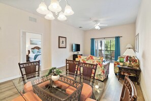 Ein Wohnzimmer mit einem Glastisch, Korbstühlen, einer Couch mit Blumenmuster, einem Deckenventilator und einem Fernseher.