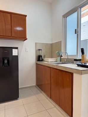 A kitchen with wooden cabinets, a black refrigerator, a blender, and a window with a view.
