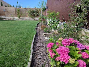 Ein gepflegter Garten mit Rasenfläche, einem Blumenbeet mit rosa Blüten und einem Holzzaun.