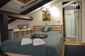 Ein Schlafzimmer mit Bett, Kissen, einem Nachttisch, einem Gemälde und einer Dusche.
