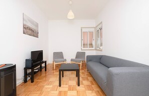 Ein Wohnzimmer mit grauem Sofa, zwei grauen Sesseln, einer schwarzen TV-Konsole, einem schwarzen Tisch und einer Pendelleuchte.