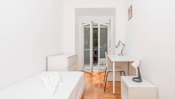 Ein Schlafzimmer mit Bett, Schreibtisch, Stuhl und Balkontür.