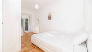Una camera da letto con un letto, un comodino, una lampada a sospensione, una finestra con vista e una porta che dà su un balcone.
