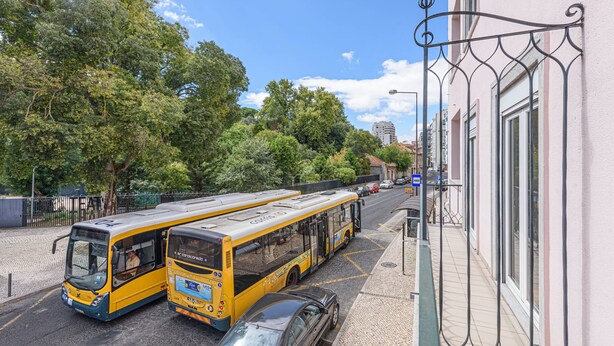 Una strada con due autobus gialli, un'auto e un edificio con un balcone in ferro battuto.