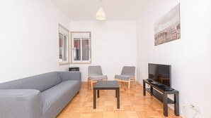Un soggiorno con un divano grigio, due poltrone, un tavolino da caffè, una televisione e un dipinto con vista sulla città.
