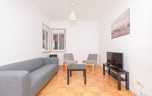 Ein Wohnzimmer mit grauem Sofa, zwei Sesseln, einem Couchtisch, einem Fernseher und einem Stadtbild.