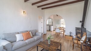 A living room with a sofa, coffee table, and a fireplace. There is a dining area with a table and chairs. - La Bailonga Cómpeta by Ruralidays (Málaga)