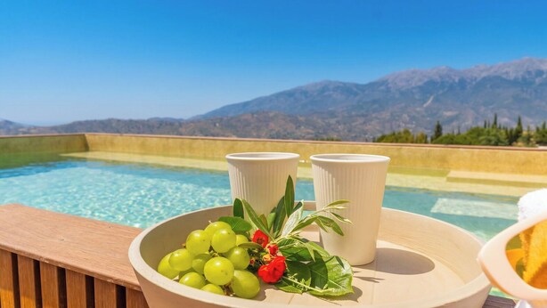 A poolside setting with a bowl of green grapes and red berries, two white cups, and a wooden deck overlooking a mountain. - La Bailonga Cómpeta by Ruralidays (Málaga)