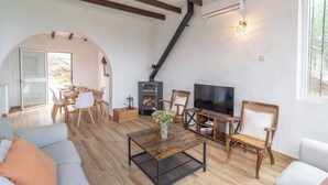 A cozy living room with a fireplace, a TV, wooden furniture, and a dining area. - La Bailonga Cómpeta by Ruralidays (Málaga)
