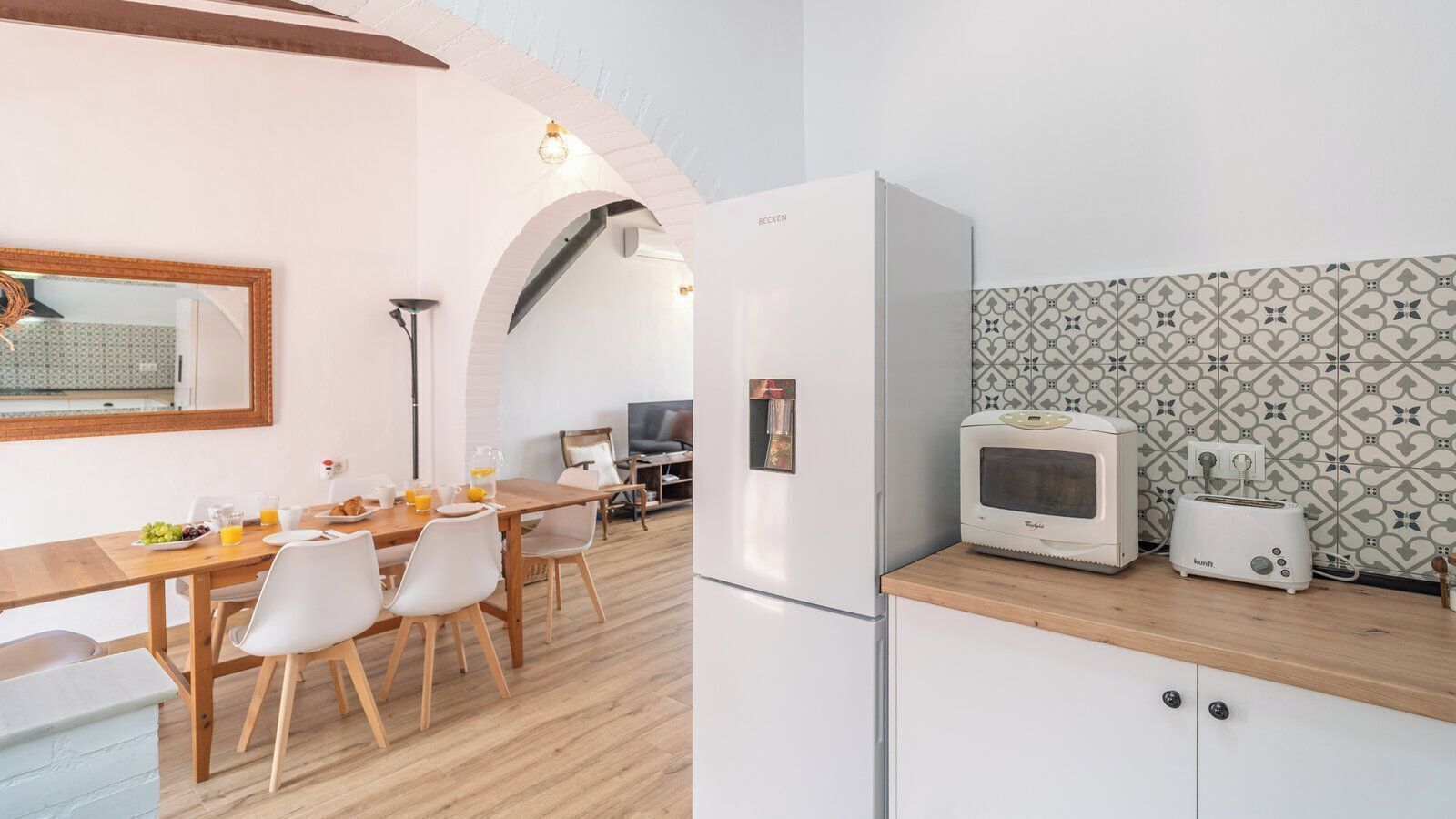 A modern kitchen with a refrigerator, microwave, and toaster, a dining area with a table and chairs, and a patterned backsplash.