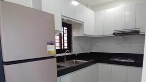 A kitchen with white cabinets, a black countertop, a stainless steel sink, and a refrigerator. - Cozy Corner Transient House (Calapan City)