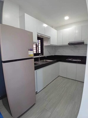 Una cocina con armarios blancos, encimera negra, pileta de acero inoxidable y refrigerador.