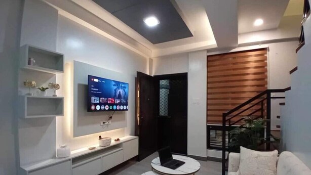 A modern living room with a flat-screen TV, white sofas, a coffee table, and a staircase. - Cozy Corner Transient House (Calapan City)
