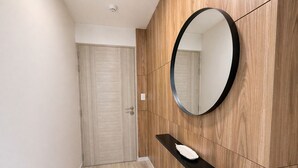 A hallway with a wooden floor, a door, a black shelf with a white object, and a round mirror on the wall. - Elegant Apartment Modern Design - 1006 (Lima)