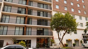 A multi-story building with balconies, a tree in the foreground, and a car parked in front. - Elegant Apartment Modern Design - 1006 (Lima)