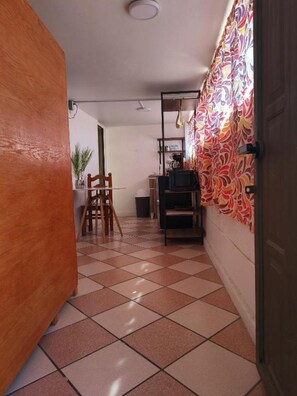 Un couloir avec un sol carrelé, une porte en bois, un coin repas avec des chaises, une table et un téléviseur posé sur un meuble.