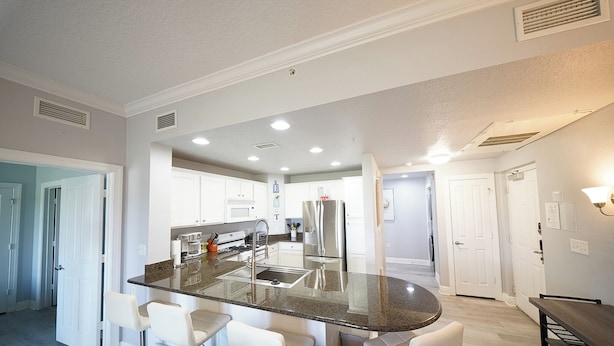 A modern kitchen with a central island, bar stools, stainless steel appliances, and recessed lighting. - Sunset Greens Retreat at Reunion-7603 (Kissimmee)