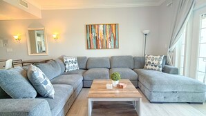A modern living room with a grey sectional sofa, a wooden coffee table, and a colorful abstract painting on the wall. - Sunset Greens Retreat at Reunion-7603 (Kissimmee)