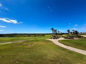 Ein Golfplatz mit blauem Himmel, Palmen und einem Weg zu einem Gebäude.
