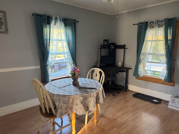 A room with a round table, chairs, a computer desk, and a window with curtains.