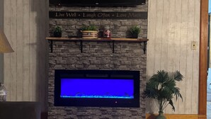 A living room with a stone fireplace, a flat-screen TV, and a fish tank.