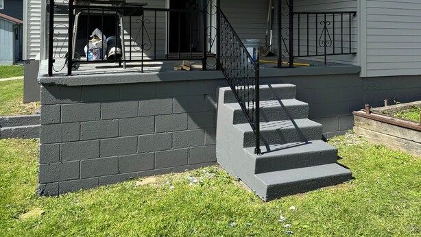 A house with a covered porch, a brick foundation, and a set of stairs leading to the entrance.