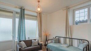 A bedroom with a bed, a sofa, a window with curtains, a wall-mounted light fixture, and a radiator. - Le Sostranien - Jardin - Wifi (La Souterraine)