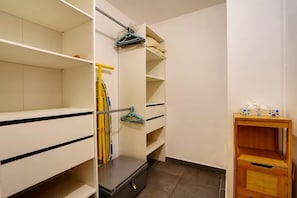 Ein Zimmer mit Schrank, einem kleinen Holztisch und einem Regal mit Kleidern.