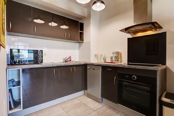 Une cuisine moderne avec des meubles de couleur sombre, un lave-vaisselle, un four et des luminaires suspendus.