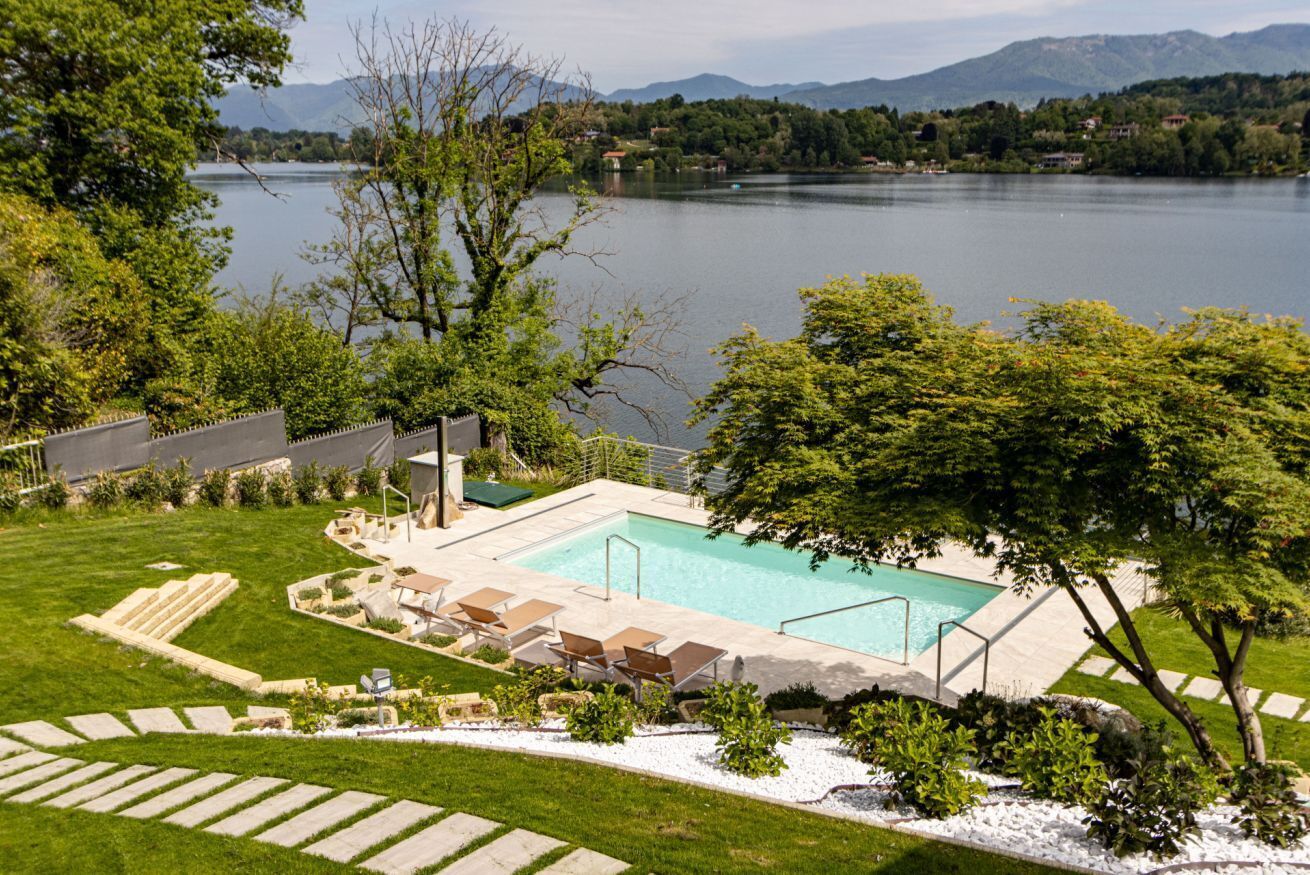 Ein Schwimmbecken mit Liegestühlen, eine Rasenfläche und Blick auf einen See und Berge.