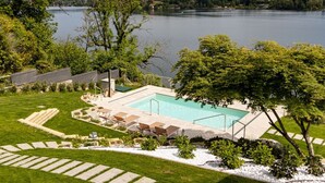 Una piscina con sillas de descanso, un césped y vistas a un lago y montañas.