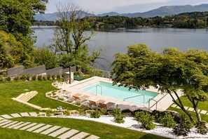 Ein Schwimmbecken mit Liegestühlen, eine Rasenfläche und Blick auf einen See und Berge.