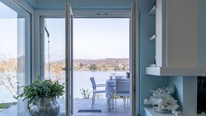 Una habitación con un ventanal grande, una planta en maceta, una mesa con sillas y una chimenea.