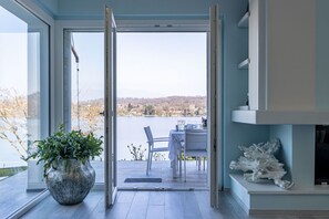 Ein Zimmer mit einem großen Fenster, einem Blumentopf, einem Tisch mit Stühlen und einem Kamin.