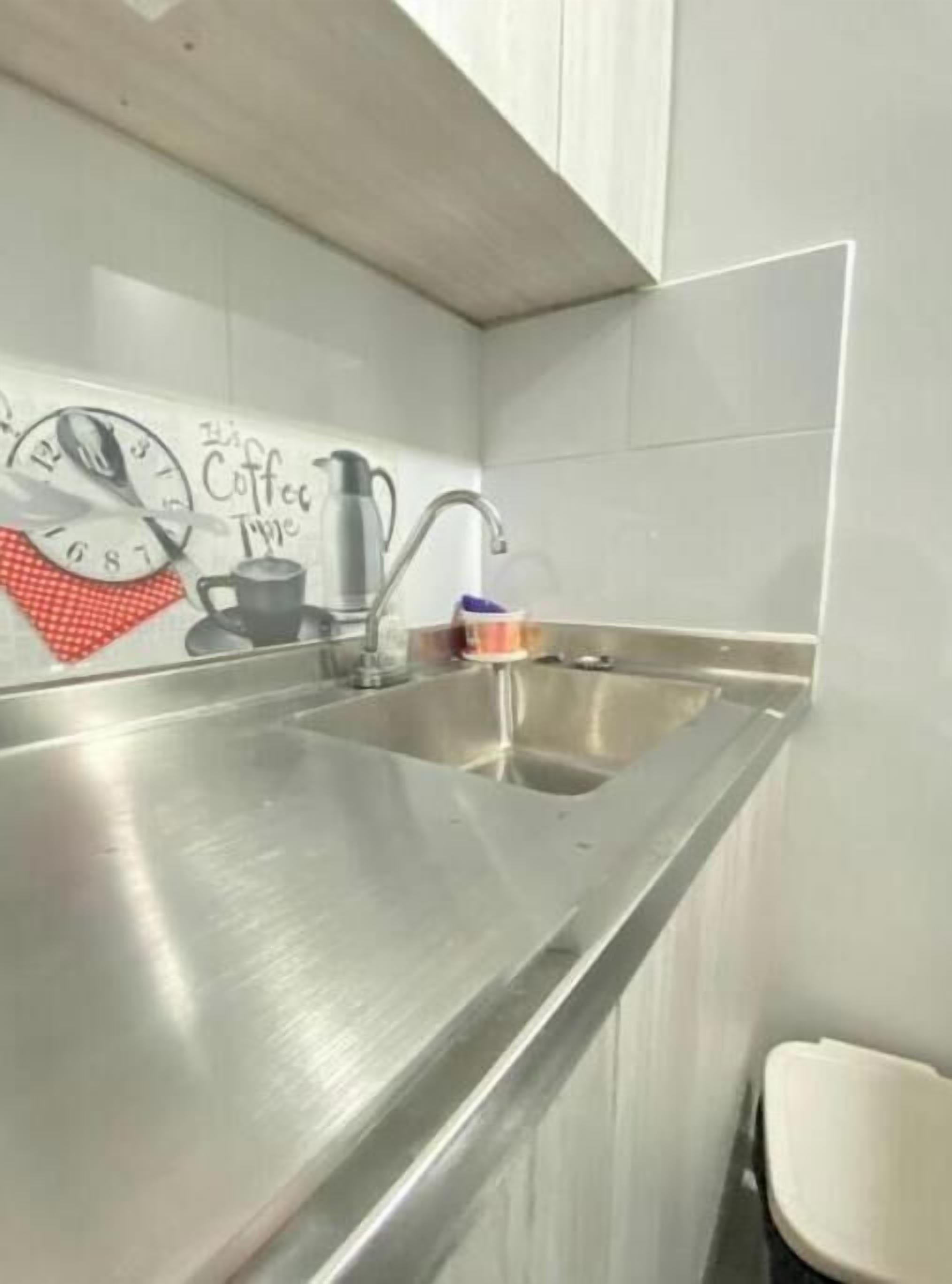 A stainless steel kitchen sink with a faucet, a coffee-themed wall decoration, and a trash bin.
