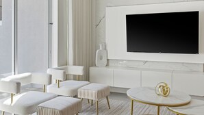 Ett modernt vardagsrum med en stor platt-TV som är monterad på en vägg av marmor, vita möbler och en glasdörr som leder ut.