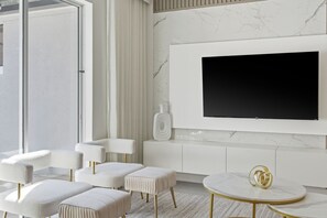 A modern living room with a large flat-screen TV mounted on a marble wall, white furniture, and a glass door leading outside. - Lovely Themed Villa w/ Private Pool | Storey Lake (2441) (Kissimmee)
