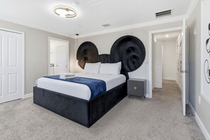 A modern bedroom with a large bed, a bedside table, a wall-mounted artwork, and a door. - Lovely Themed Villa w/ Private Pool | Storey Lake (2441) (Kissimmee)