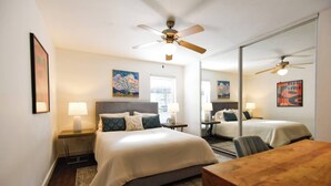 A bedroom with two beds, a wooden table, a ceiling fan, and artwork on the walls. - The Hidden Gem of Dallas (Dallas)