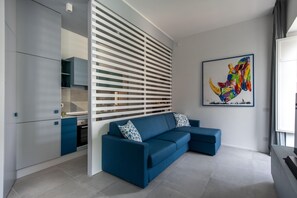 A modern living room with a blue sofa, a kitchen area, and a colorful artwork on the wall. - Azul Balcony near the Cala (PALERMO)