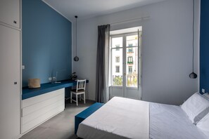A bedroom with a bed, a desk, a chair, and a window with a view of buildings. - Azul Balcony near the Cala (PALERMO)