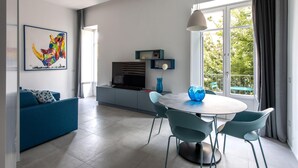 Un salon moderne avec un canapé bleu, une table à manger avec des chaises, un téléviseur et une grande fenêtre donnant sur un paysage verdoyant.
