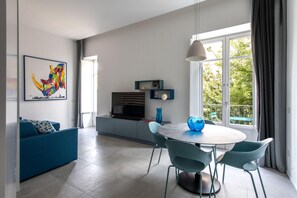 A modern living room with a blue sofa, a dining table with chairs, a TV, and a large window with a view of greenery. - Azul Balcony near the Cala (PALERMO)