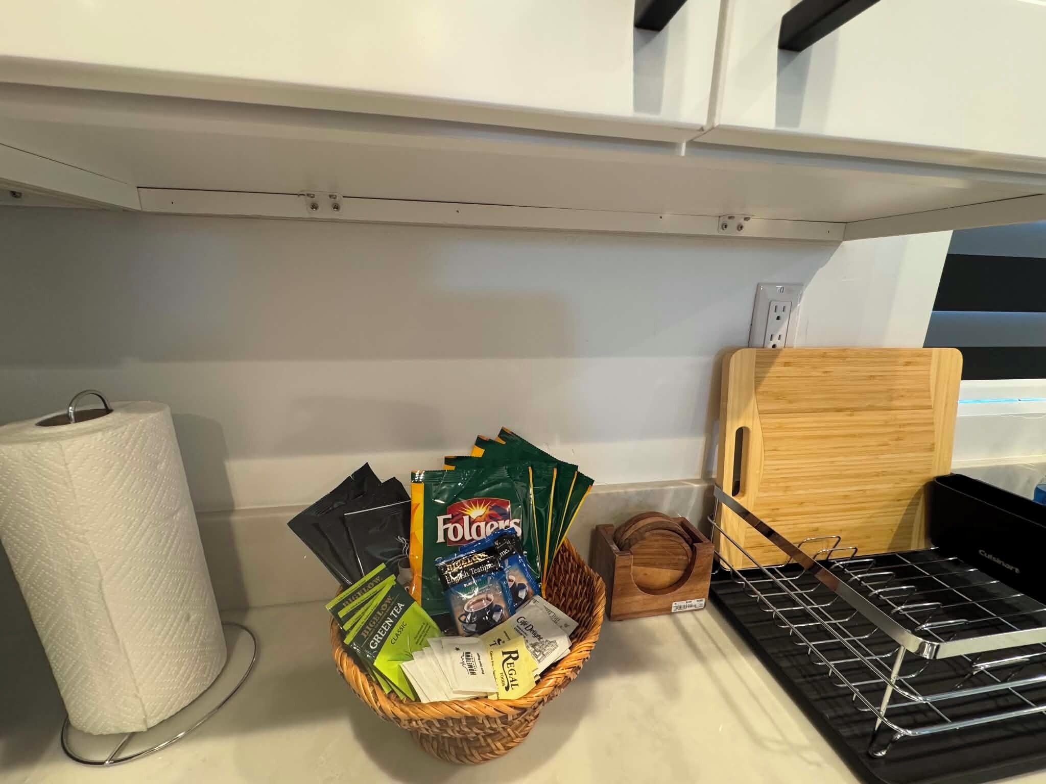 A kitchen counter with a basket of tea bags, a roll of paper towels, and a cutting board.