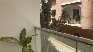 Ein Balkon mit einer Topfpflanze, einem Glasgeländer und Blick auf eine Straße und Gebäude.