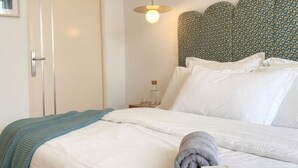 Ein ordentlich bezogenes Bett mit weißen Leinen, ein graues Handtuch und eine Willkommenskarte.