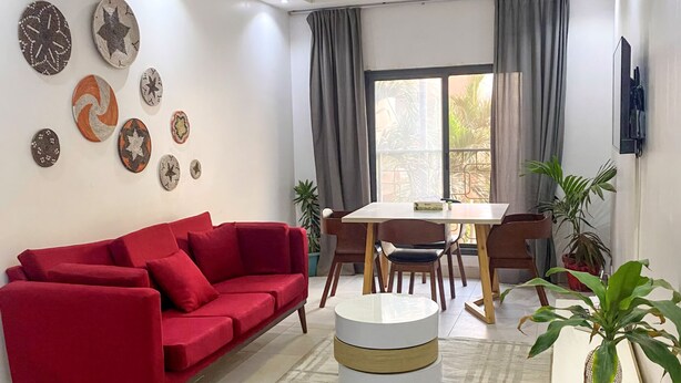 Ein modernes Wohnzimmer mit einem roten Sofa, einem Esstisch mit Stühlen, einem runden Couchtisch und einer Zimmerpflanze.
