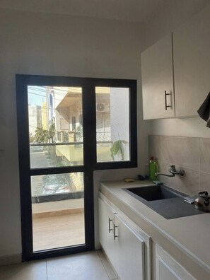 A kitchen with a large window, a sink, cabinets, and a plant. - Cozy 2-bedroom apartment with AC and hot water in Dakar (Dakar)
